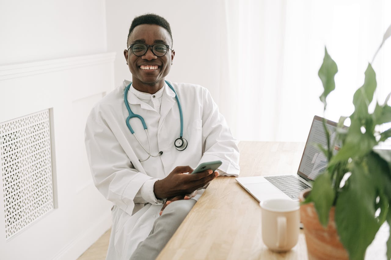 a doctor smiling and using his phone and laptop